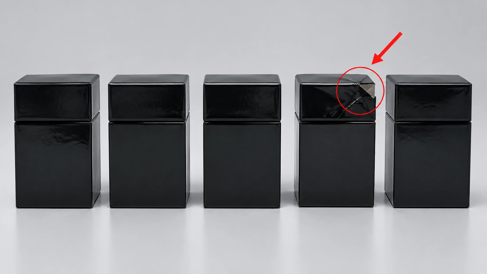 Row of identical black two-piece rigid boxes where one box has a crushed corner highlighted by a red circle and a red diagonal arrow