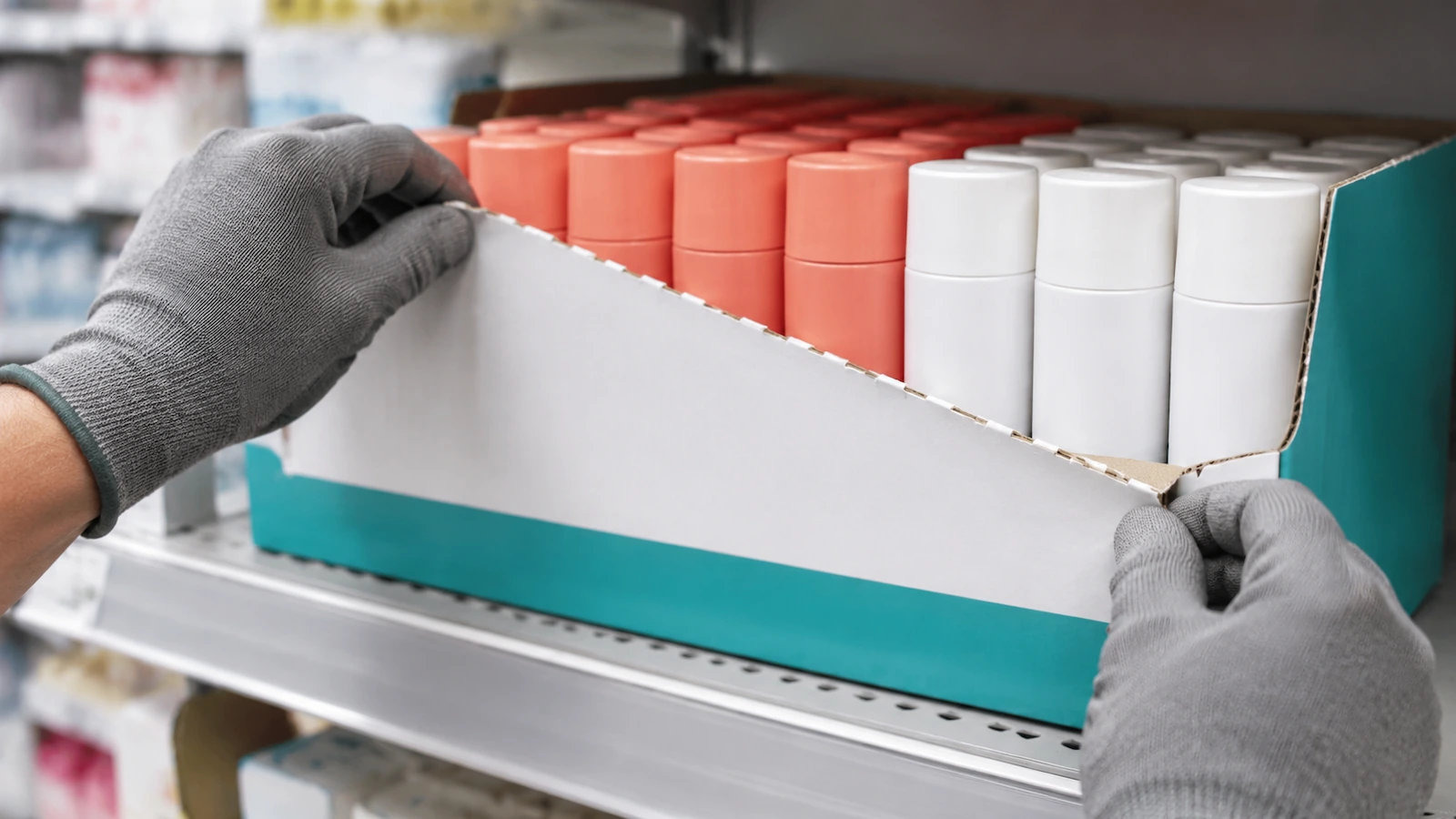 Hands removing the perforated front panel of a corrugated shelf-ready tray, revealing neatly arranged product ready for the shelf