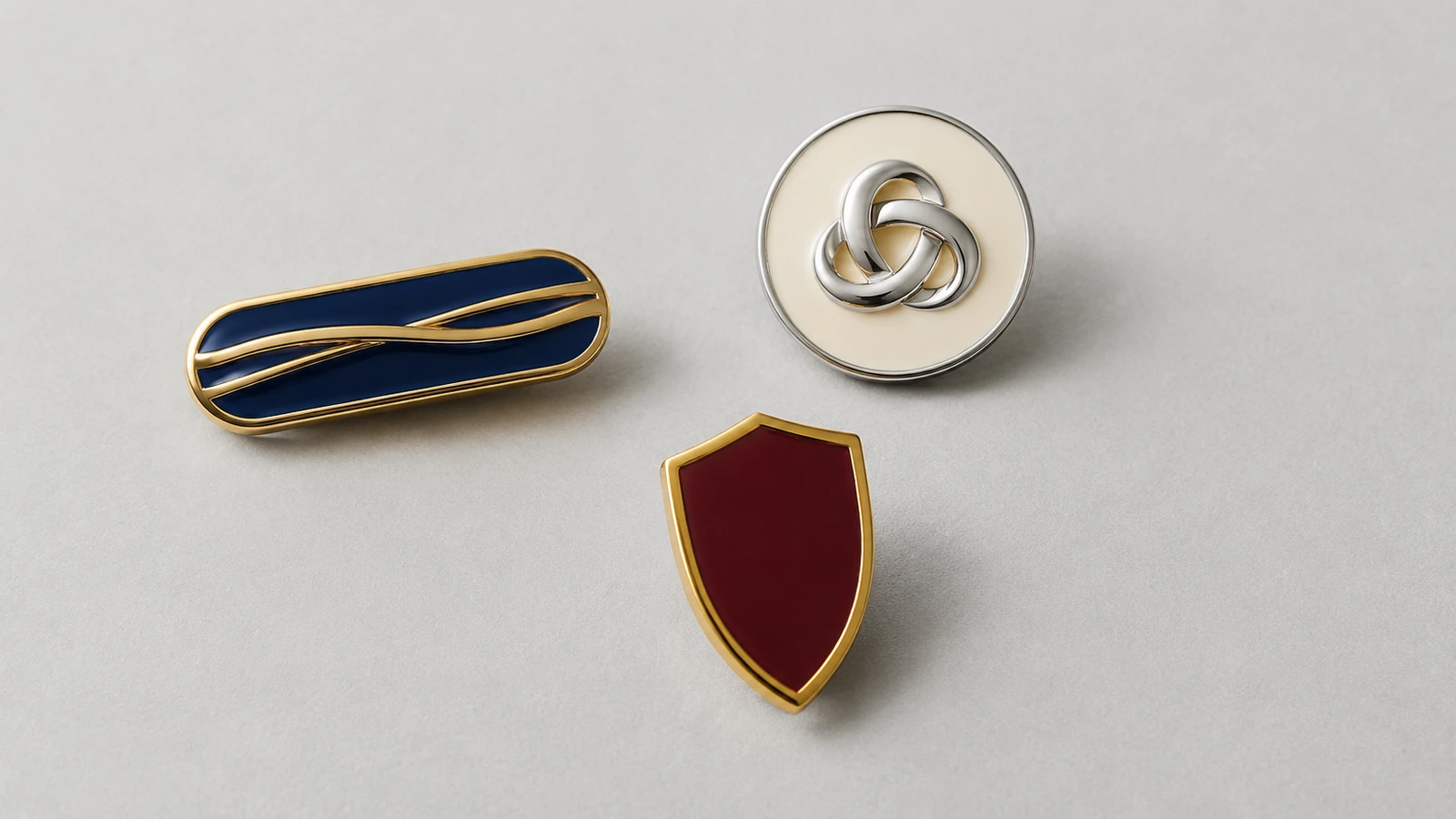 Minimal blank pins with smooth raised metal ribbons and an interlocking loop shape that suggest typography without any readable characters
